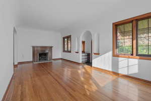 Unfurnished living room featuring arched walkways, wood finished floors, and a high end fireplace