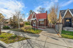 Tudor home featuring brick siding, a fenced front yard, a chimney, and concrete driveway
