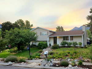 Tri-level home featuring a front yard, a chimney, brick siding, and a shingled roof