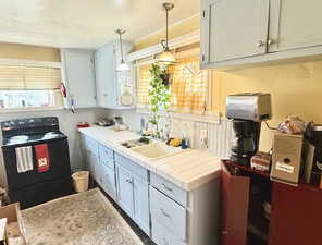 Kitchen featuring black range with electric stovetop, pendant lighting, and tile countertops