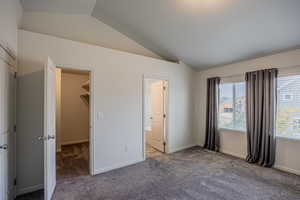 Unfurnished bedroom with vaulted ceiling, carpet flooring, a walk in closet, and connected bathroom