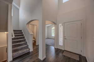 Foyer with arched walkways, stairway, a high ceiling, and dark wood-style flooring
