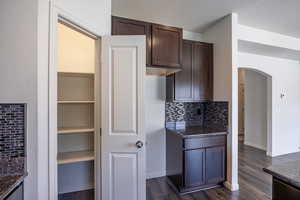Kitchen featuring arched walkways, dark brown cabinets, tasteful backsplash, dark wood-style floors, and a textured ceiling