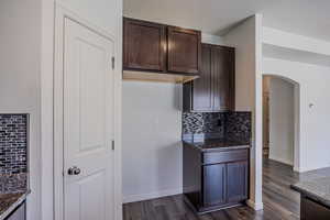 Kitchen with arched walkways, decorative backsplash, dark brown cabinetry, dark wood finished floors, and a textured ceiling