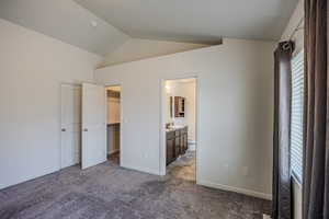 Unfurnished bedroom featuring vaulted ceiling, carpet flooring, ensuite bath, and a walk in closet