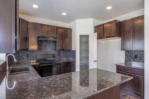 Kitchen featuring backsplash, black electric range oven, dark brown cabinets, dark stone counters, and recessed lighting