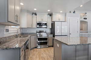 Kitchen featuring gray cabinets, stainless steel appliances, arched walkways, dark stone counters, and recessed lighting