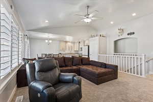 Living room featuring vaulted ceiling, carpet flooring, a ceiling fan, a chandelier, and healthy amount of natural light