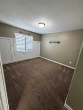 Empty room with dark colored carpet and a textured ceiling