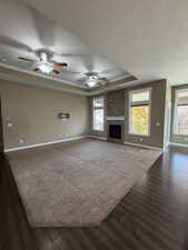 Unfurnished living room featuring a raised ceiling, a stone fireplace, a ceiling fan, dark wood-style floors, and a textured ceiling