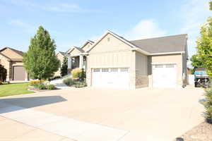 Craftsman inspired home with board and batten siding, stone siding, a garage, and driveway