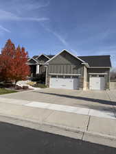 Craftsman-style house featuring board and batten siding, stone siding, concrete driveway, an attached garage, and roof with shingles