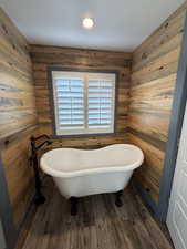 Bathroom featuring dark wood-style flooring, a soaking tub, and wooden walls