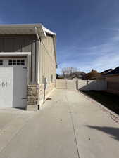 View of property exterior with stone siding, a gate, concrete driveway, and board and batten siding