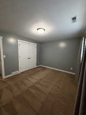 Unfurnished bedroom with dark carpet, a textured ceiling, and a closet