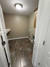 Washroom featuring a textured ceiling, cabinet space, dark stone finish flooring, hookup for an electric dryer, and hookup for a washing machine