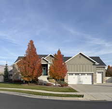 View of front facade featuring board and batten siding, stone siding, driveway, an attached garage, and a front yard