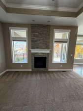 Unfurnished living room with crown molding, healthy amount of natural light, a tray ceiling, and a stone fireplace