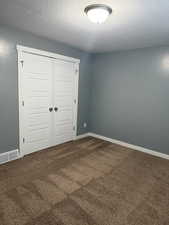 Unfurnished bedroom with dark colored carpet, a closet, and a textured ceiling