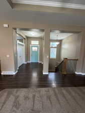 Foyer with dark wood finished floors, dark carpet, and crown molding