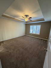 Spare room featuring a tray ceiling, dark carpet, a textured ceiling, a ceiling fan, and crown molding