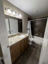 Bathroom featuring vanity, shower / bathtub combination with curtain, a textured ceiling, and stone tile flooring