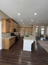 Kitchen featuring light stone counters, stainless steel appliances, a center island with sink, dark wood-type flooring, and a kitchen bar
