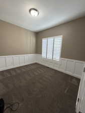 Spare room with a decorative wall, a wainscoted wall, a textured ceiling, and dark colored carpet