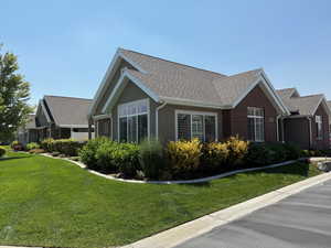 View of side of property featuring a shingled roof, a yard, and brick siding