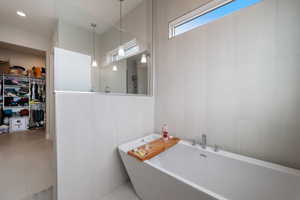 Bathroom featuring a soaking tub, tile walls, a walk in closet, and tile patterned flooring