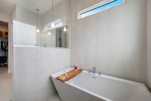 Full bathroom with a soaking tub, tile walls, and a walk in closet