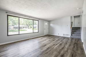 Unfurnished living room featuring a textured ceiling, stairway, and wood finished floors