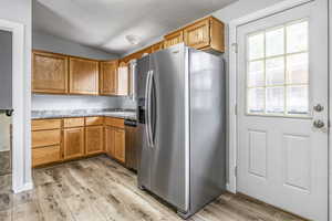 Kitchen featuring appliances with stainless steel finishes, light wood-style flooring, vaulted ceiling, light countertops, and brown cabinets