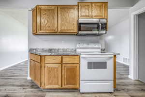 Kitchen with white electric range, stainless steel microwave, light wood-style floors, and brown cabinetry