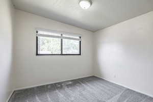 Carpeted empty room with lofted ceiling and baseboards