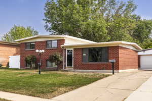 Tri-level home with brick siding, a front lawn, driveway, a detached garage, and an outbuilding