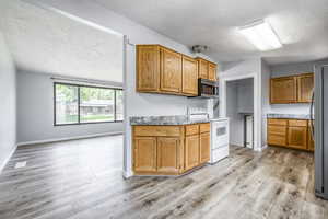 Kitchen with appliances with stainless steel finishes, a textured ceiling, light wood-type flooring, brown cabinets, and stone counters