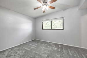 Carpeted empty room with vaulted ceiling and a ceiling fan