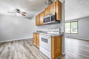 Kitchen featuring white range with electric stovetop, a textured ceiling, stainless steel microwave, light wood-style floors, and a ceiling fan