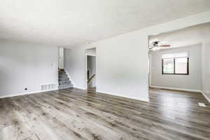 Unfurnished room featuring wood finished floors, ceiling fan, and stairs