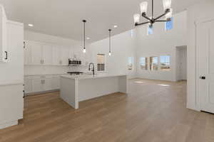 Kitchen with a chandelier, light wood-style floors, light countertops, decorative backsplash, and a center island with sink