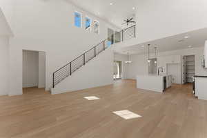 Unfurnished living room featuring light wood-type flooring, stairs, ceiling fan, a chandelier, and recessed lighting