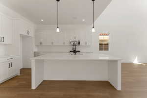 Kitchen with white cabinetry, a kitchen island with sink, light wood-style floors, light countertops, and backsplash
