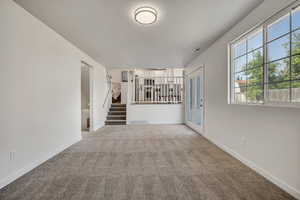 Unfurnished living room featuring carpet flooring, stairway, and french doors