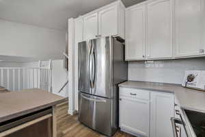Kitchen featuring appliances with stainless steel finishes, white cabinetry, wood finished floors, and decorative backsplash