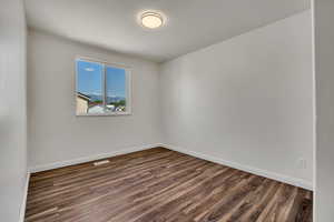 Spare room featuring dark wood-style floors and baseboards