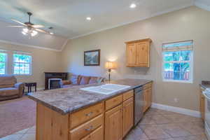 Kitchen featuring crown molding, lofted ceiling, light tile patterned floors, dishwasher, and light brown cabinetry