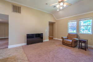 Living area with ornamental molding, vaulted ceiling, carpet floors, a ceiling fan, and tile patterned floors
