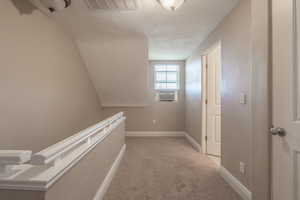 Hallway featuring light carpet, a textured ceiling, and vaulted ceiling