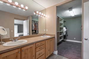 Ensuite bathroom with a textured ceiling, double vanity, a spacious closet, and tile patterned flooring